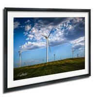 A framed photograph depicting a field with multiple wind turbines against a blue sky with clouds.