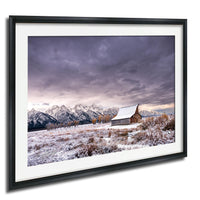 A snowy mountain landscape with a wooden barn in the foreground, set against a dramatic cloudy sky.