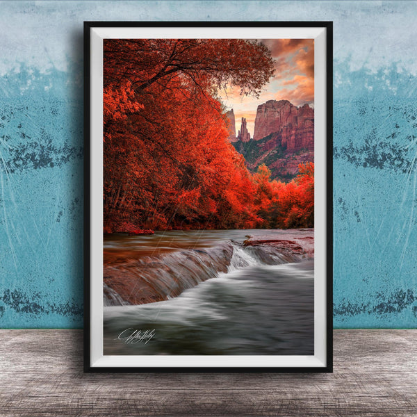 A framed photograph depicting a serene landscape with a waterfall cascading over rocks, surrounded by vibrant red foliage and set against a backdrop of towering red rock formations.