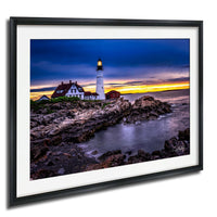 A framed photograph depicting a lighthouse on a rocky shore at sunset, with the sky filled with vibrant colors.