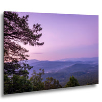 a breathtaking view of a mountainous landscape at sunset, with the sky painted in shades of purple and pink. The mountains in the distance are covered in lush green trees, creating a serene and picturesque scene.
