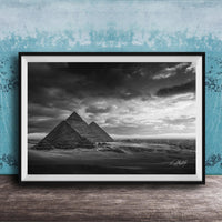A black and white photograph of the iconic pyramids of Giza in Egypt, set against a dramatic cloudy sky.