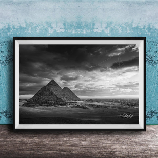 A black and white photograph of the iconic pyramids of Giza in Egypt, set against a dramatic cloudy sky.