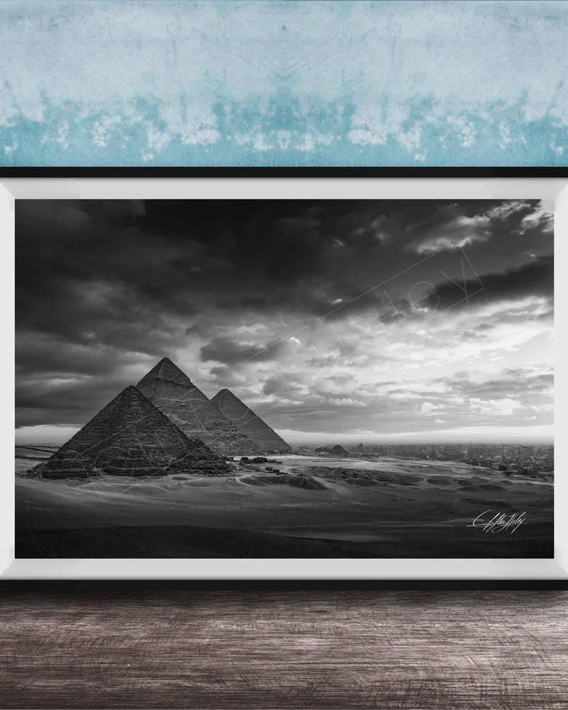 A black and white photograph of the iconic pyramids of Giza in Egypt, set against a dramatic cloudy sky.