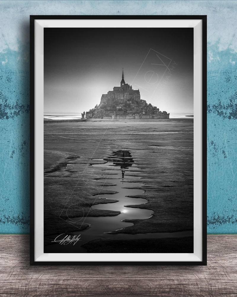 A black and white photograph of a castle or palace situated on a beach, with a body of water in the foreground and a sky above.
