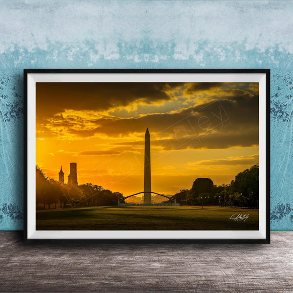 the Washington Monument at sunset, with the tall obelisk silhouetted against a vibrant orange and yellow sky.