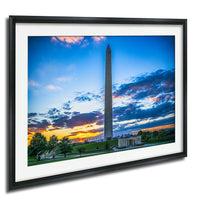 a tall obelisk against a colorful sunset sky, with a building and trees in the foreground.