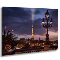 a nighttime view of the Eiffel Tower in Paris, France, with its iconic structure illuminated against a dark sky. The tower is surrounded by ornate street lamps and other architectural elements, creating a picturesque scene.