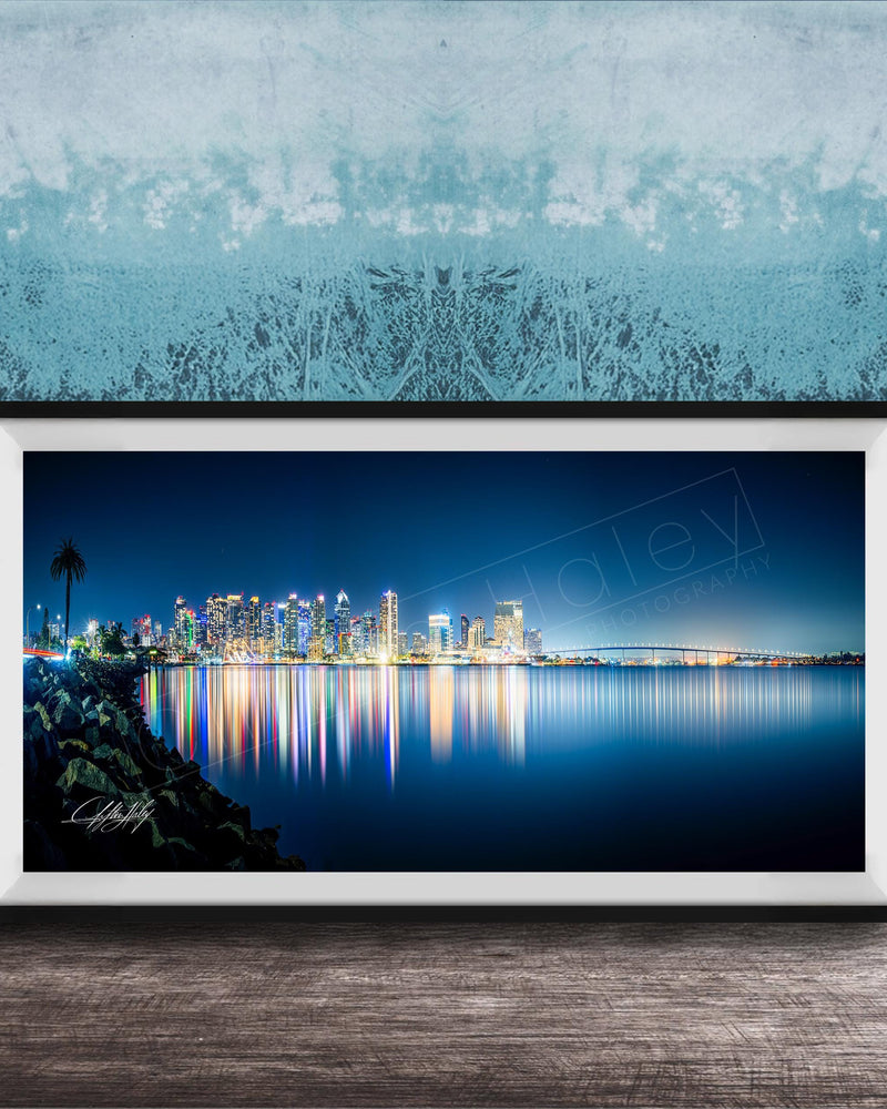 A framed photograph of a city skyline at night, with the city's lights reflected in the water below.