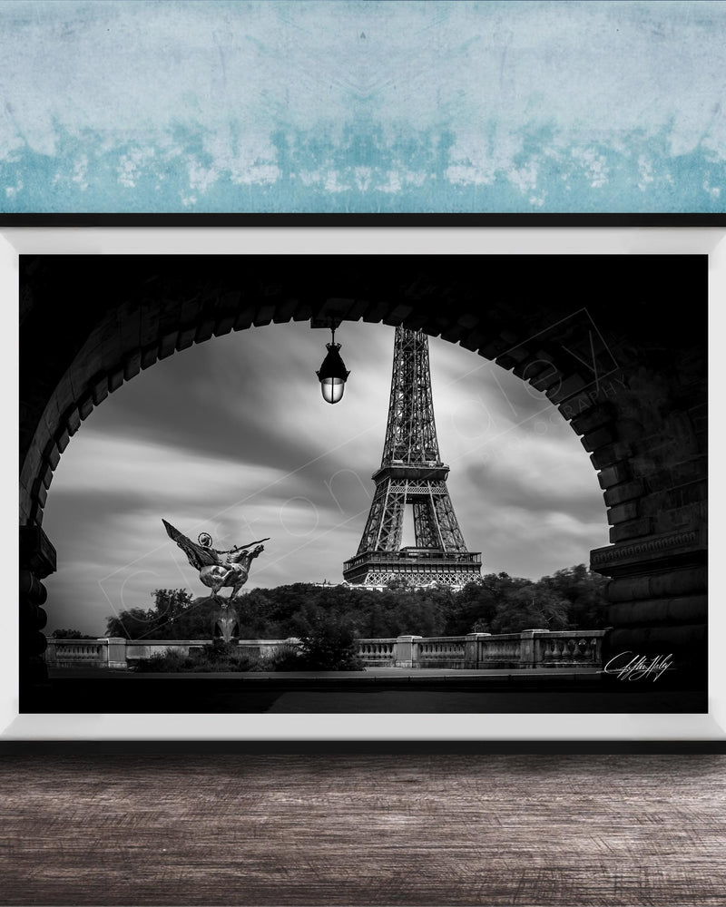 A black and white photograph of the Eiffel Tower in Paris, France, framed and displayed on a wooden surface against a blue textured wall.