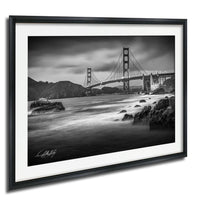 A black and white photograph of the Golden Gate Bridge in San Francisco, California, with the bridge's distinctive towers and suspension cables spanning the bay.