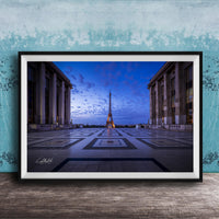 a large, framed photograph of the Eiffel Tower in Paris, France, with the tower illuminated against a blue sky.