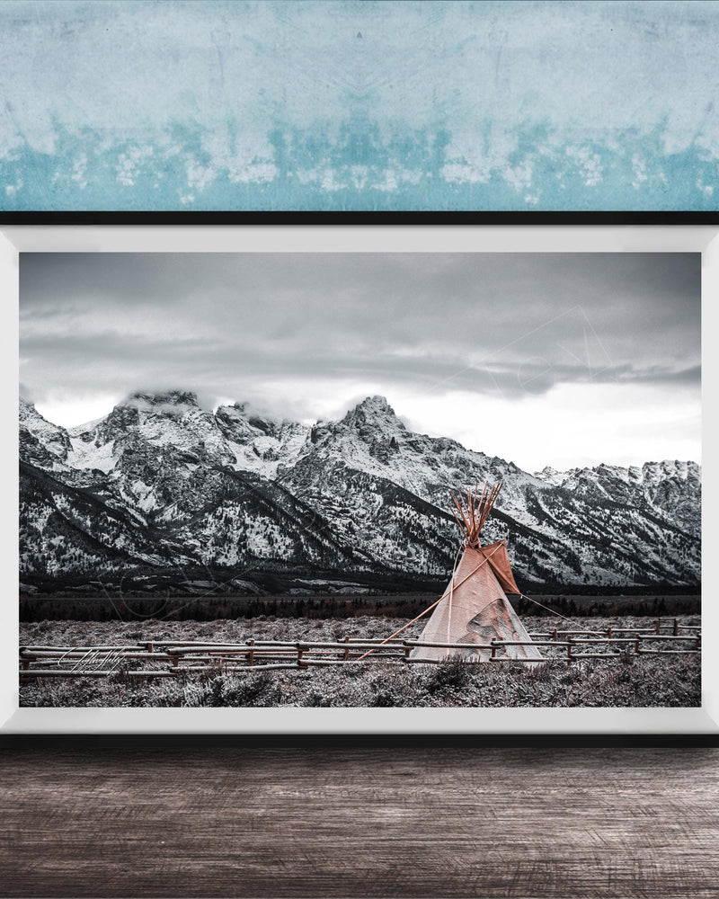 A framed photograph of a teepee in a snowy mountain landscape, with a blue wall in the background.