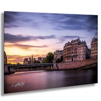 a picturesque cityscape with a river running through it, featuring a bridge and buildings with ornate architecture. The sky is filled with clouds, creating a dramatic backdrop for the scene. The colors in the image are vibrant, with the warm hues of the setting sun casting a golden glow over the city.