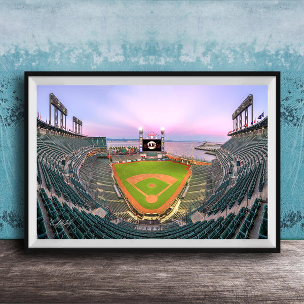 A framed photograph of a baseball stadium at dusk, with the field illuminated and the sky displaying a colorful sunset.