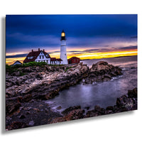 A picturesque coastal scene at sunset, featuring a lighthouse on a rocky shore with a house and a red building in the background. The sky is filled with vibrant colors, creating a stunning backdrop for the lighthouse and the surrounding landscape.