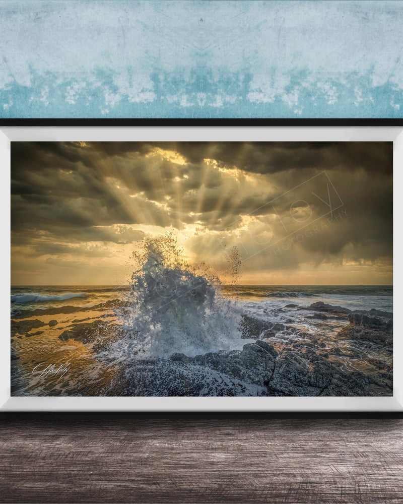 The image is a framed photograph of a dramatic ocean scene, with crashing waves and a dramatic sky filled with clouds and sunbeams.