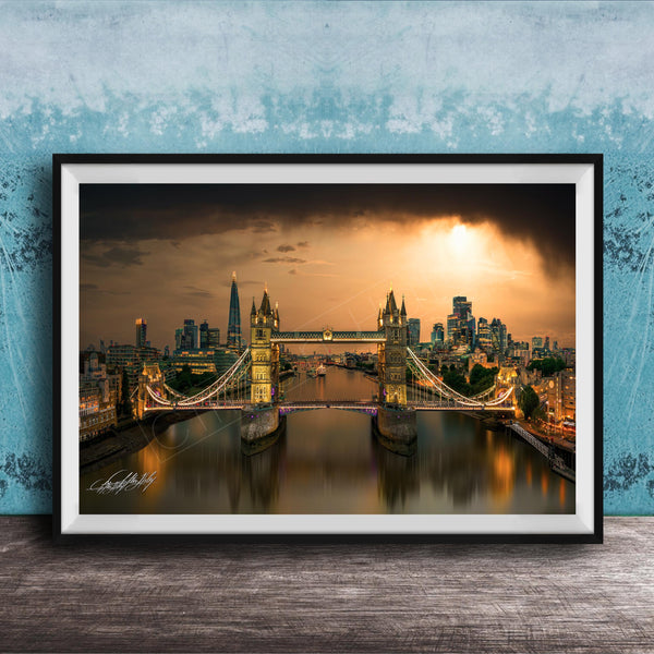 A framed photograph of the Tower Bridge in London, England, with the city skyline and the River Thames in the background, illuminated by a warm, golden glow.