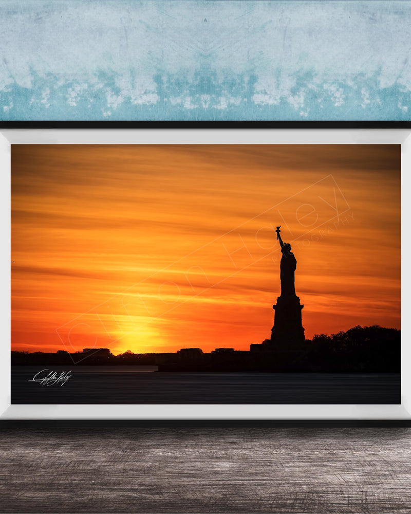 A framed photograph of the Statue of Liberty silhouetted against a vibrant sunset sky.
