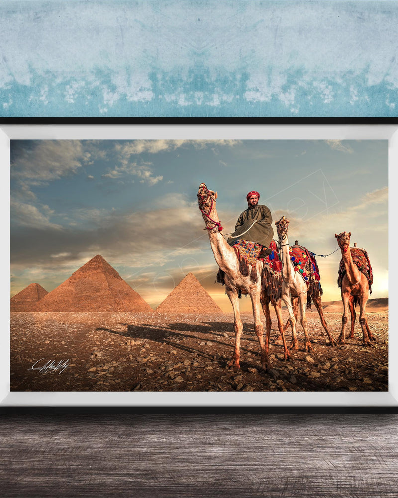 A framed photograph depicting a camel caravan in front of the iconic pyramids of Giza, Egypt, with a man riding one of the camels.