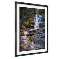 A framed photograph depicting a waterfall cascading down a rocky cliff surrounded by trees with autumn foliage.