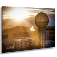 a city skyline at sunset, with a large tower in the foreground and a mountain range in the background.