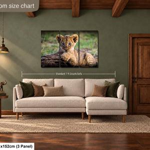 a living room with a large sofa, a wooden door, and a painting of a young lion resting on a log. The painting is hung on the wall above the sofa, and the living room appears to be well-lit and decorated.