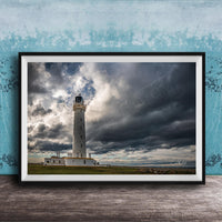 A framed photograph of a lighthouse against a stormy sky, with the lighthouse standing tall on a grassy field.