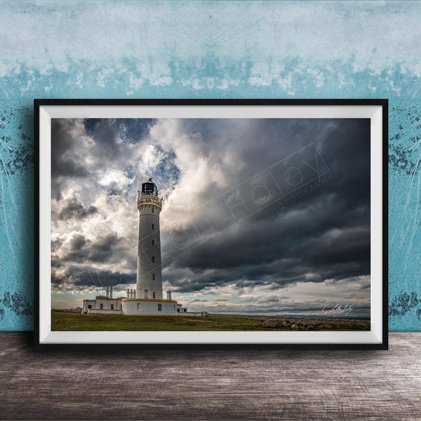 A framed photograph of a lighthouse against a stormy sky, with the lighthouse standing tall on a grassy field.