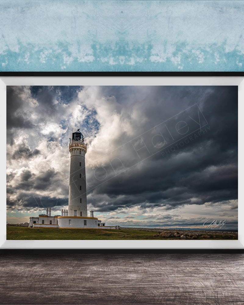 A framed photograph of a lighthouse against a stormy sky, with the lighthouse standing tall on a grassy field.