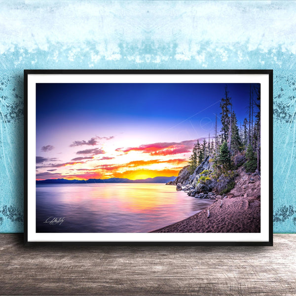 A framed photograph depicting a serene landscape with a calm lake reflecting the vibrant colors of a sunset sky, surrounded by trees and mountains.