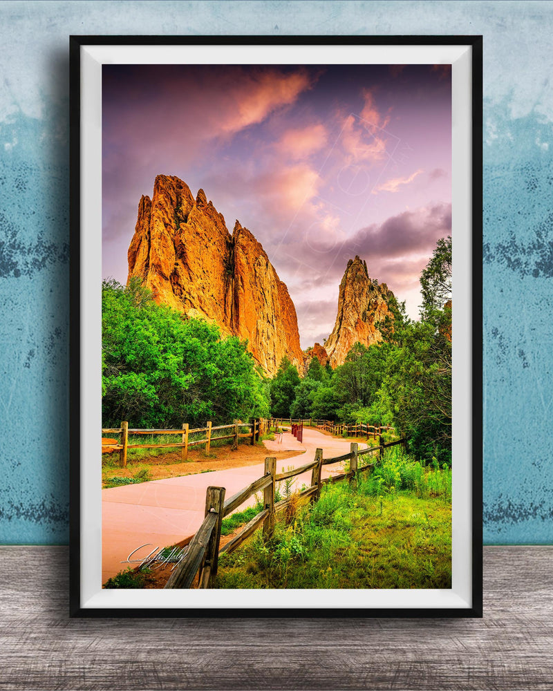 A framed photograph of a scenic landscape with towering rock formations, a wooden fence, and a vibrant sky with clouds.