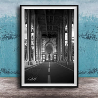 A black and white photograph of a long, narrow hallway with tall columns and arches, leading to a doorway at the end. The hallway appears to be part of a larger architectural structure, possibly a building or a church.