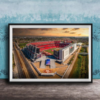 The image is an aerial view of a large sports stadium, likely the 49ers stadium, with its distinctive red roof and surrounding landscape.