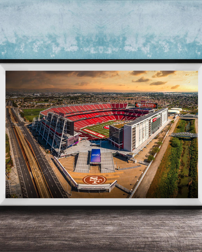 The image is an aerial view of a large sports stadium, likely the 49ers stadium, with its distinctive red roof and surrounding landscape.