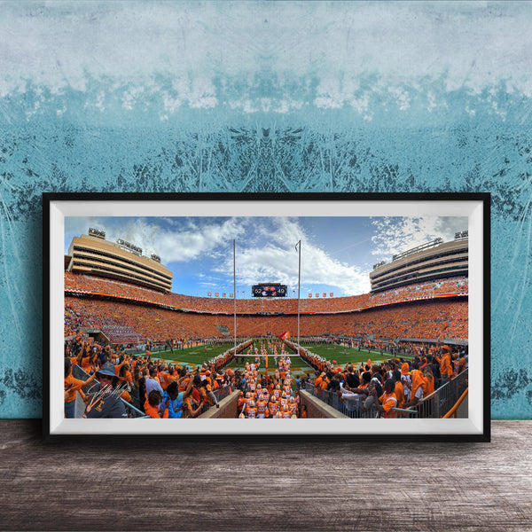 A framed photograph of a crowded football stadium with a large crowd of spectators, a large scoreboard, and a large field.