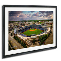 An aerial view of a baseball stadium with a lush green field, surrounded by buildings and a cloudy sky.