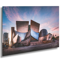 a modern, curved building with a metallic, angular design set against a colorful sky at sunset.