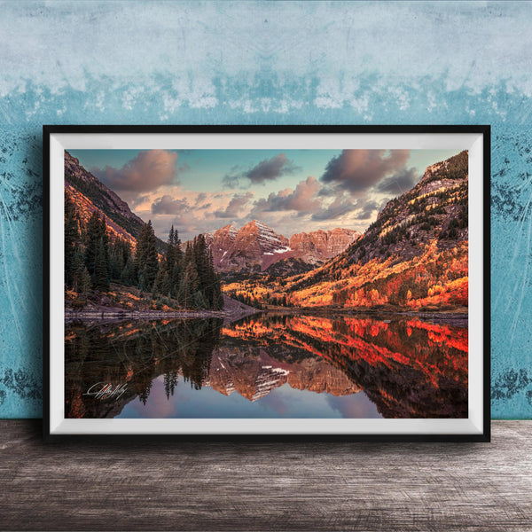 The image is a framed photograph depicting a scenic mountain landscape with a lake reflecting the mountains and trees.
