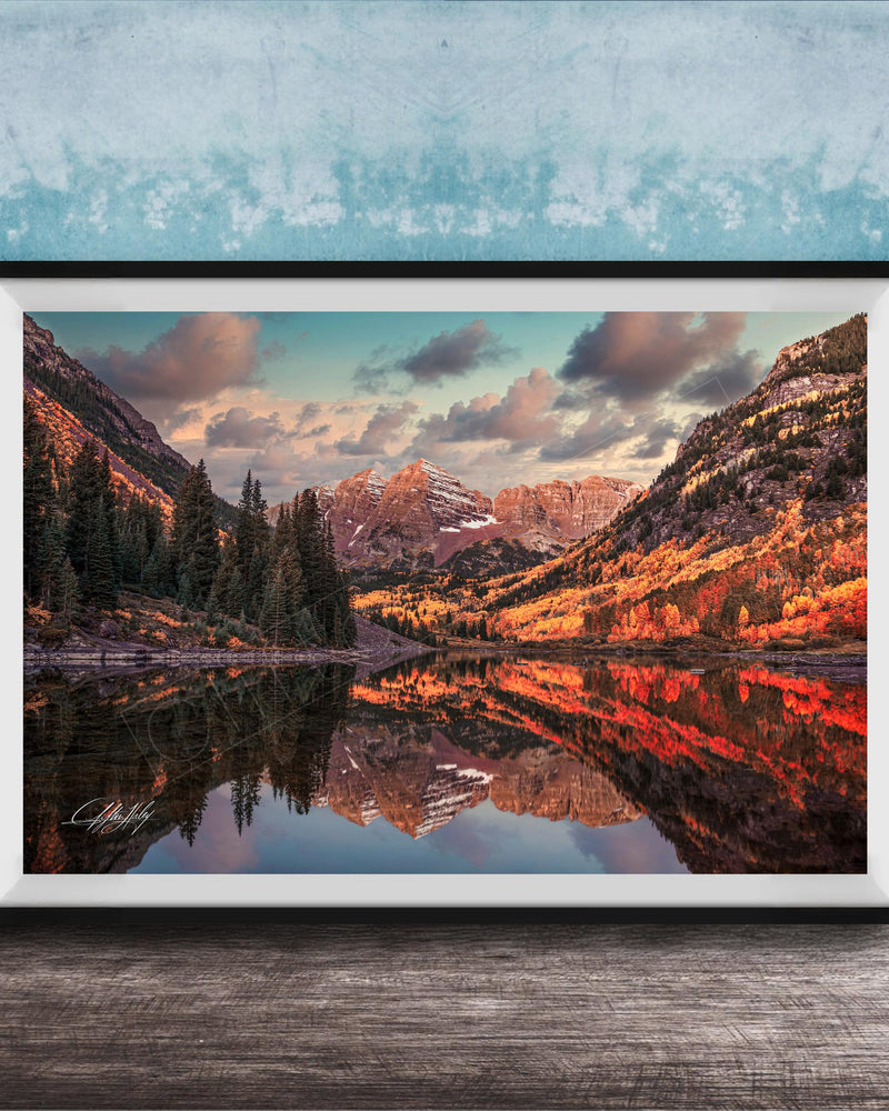 The image is a framed photograph depicting a scenic mountain landscape with a lake reflecting the mountains and trees.