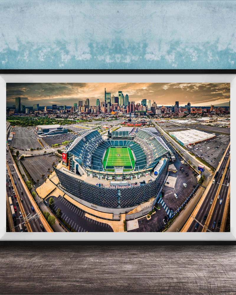 An aerial view of a large sports stadium surrounded by a city skyline, with the stadium's green field and surrounding parking lots visible.