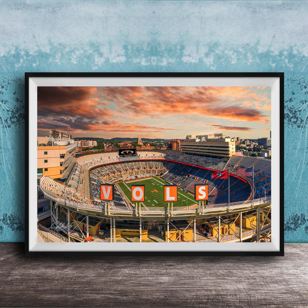 A framed photograph of a sports stadium with the word "VOLS" prominently displayed, set against a backdrop of a colorful sunset sky.