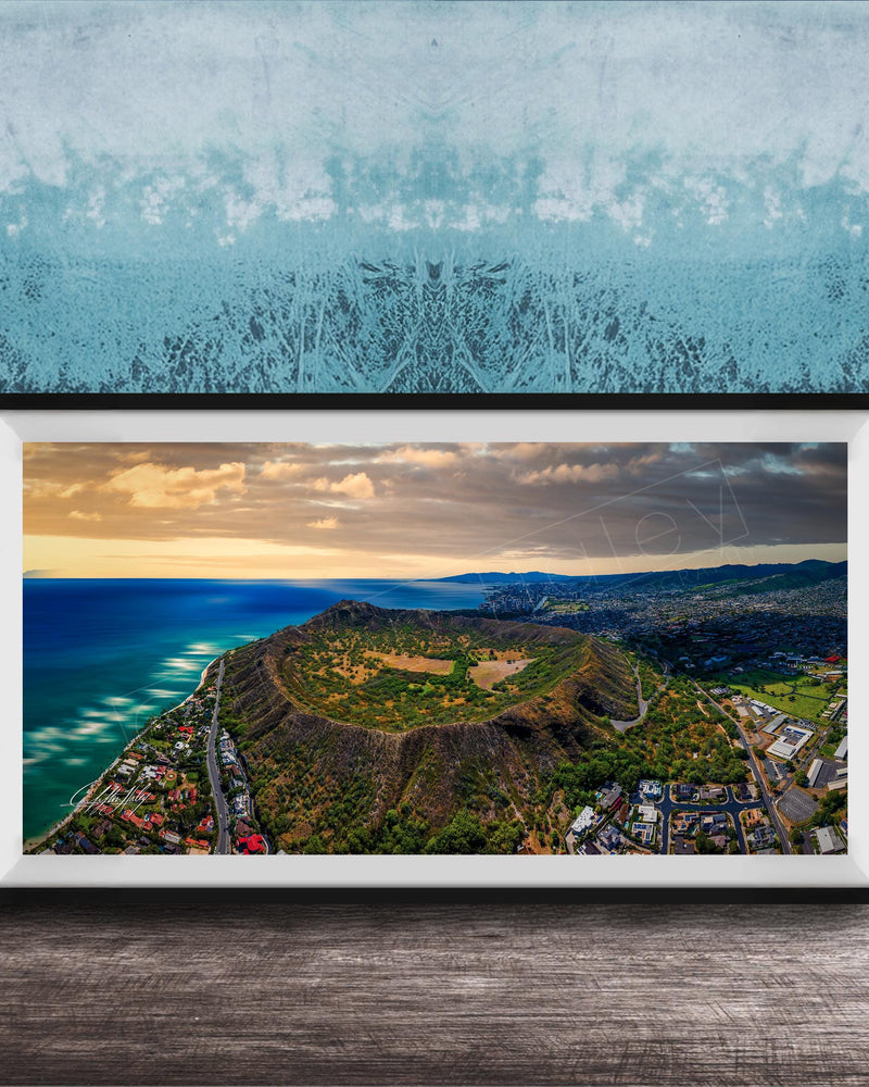 The image is a framed aerial view of a mountainous landscape with a coastal area, featuring a mix of green, brown, and blue colors.