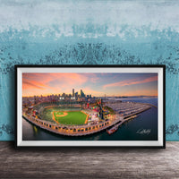 A framed aerial view of a baseball stadium and its surrounding cityscape at sunset.