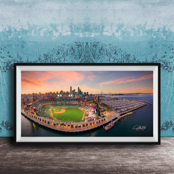 A framed aerial view of a baseball stadium and its surrounding cityscape at sunset.