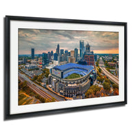 The image is an aerial view of a city skyline, featuring a large stadium with a blue roof and surrounding buildings.