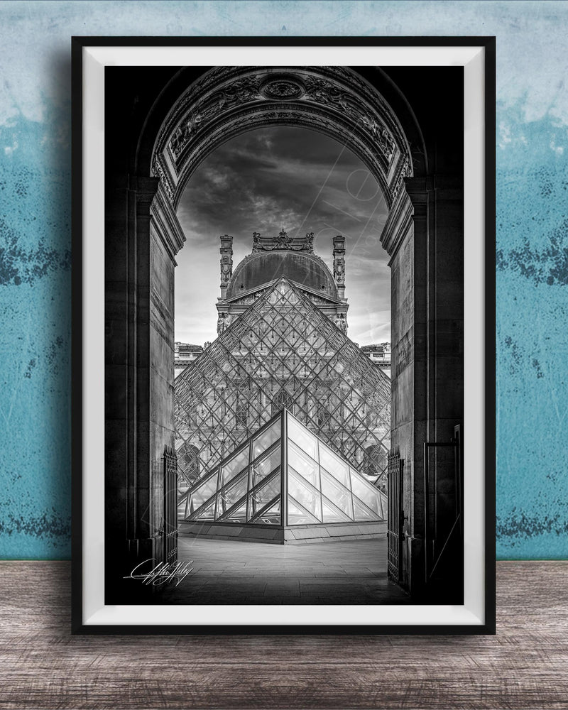 A framed photograph of the Louvre Museum in Paris, France, with the iconic glass pyramid structure prominently featured in the center of the frame.