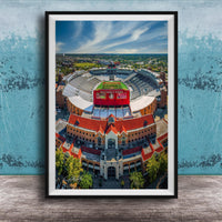 The image is an aerial view of a large stadium with a red roof, surrounded by buildings and a green field.
