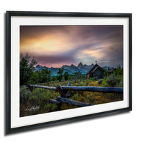 a serene rural landscape with a wooden fence, a small wooden building, and a mountain range in the background, all under a colorful sunset sky.