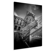 A black and white photograph of the Louvre Museum in Paris, France, featuring the iconic Louvre Pyramid and the surrounding architecture.